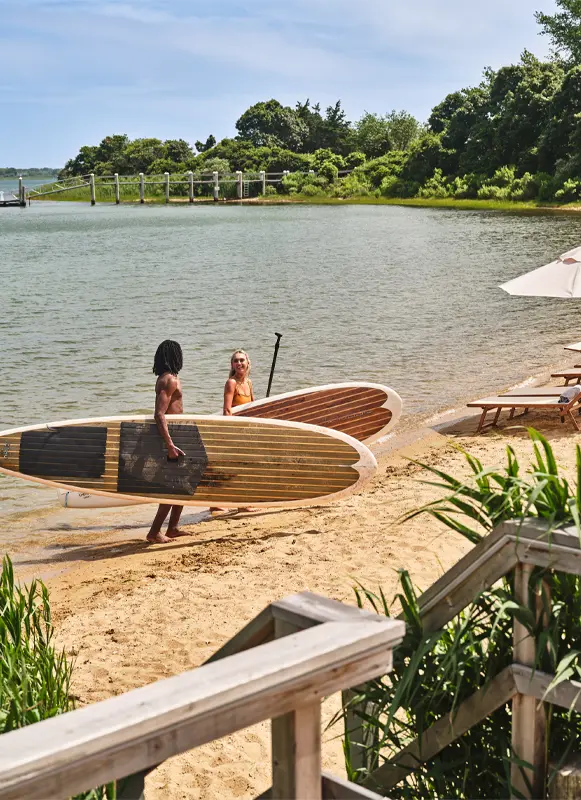 two people carrying paddle boards on the beach