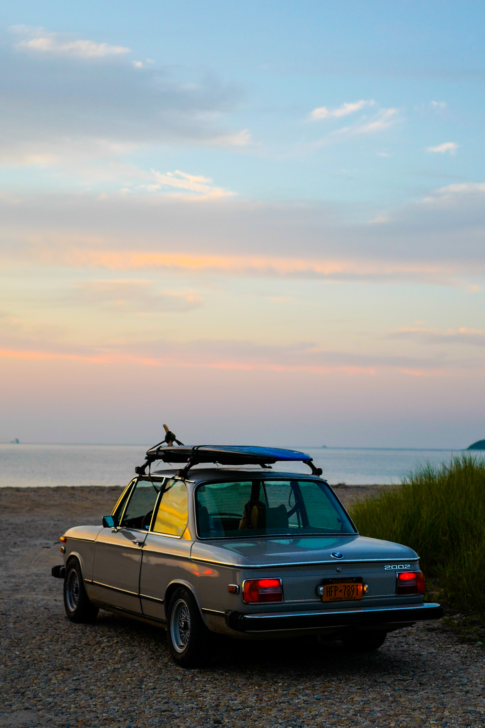 A BMW car is parked on the beach near a grassy area.