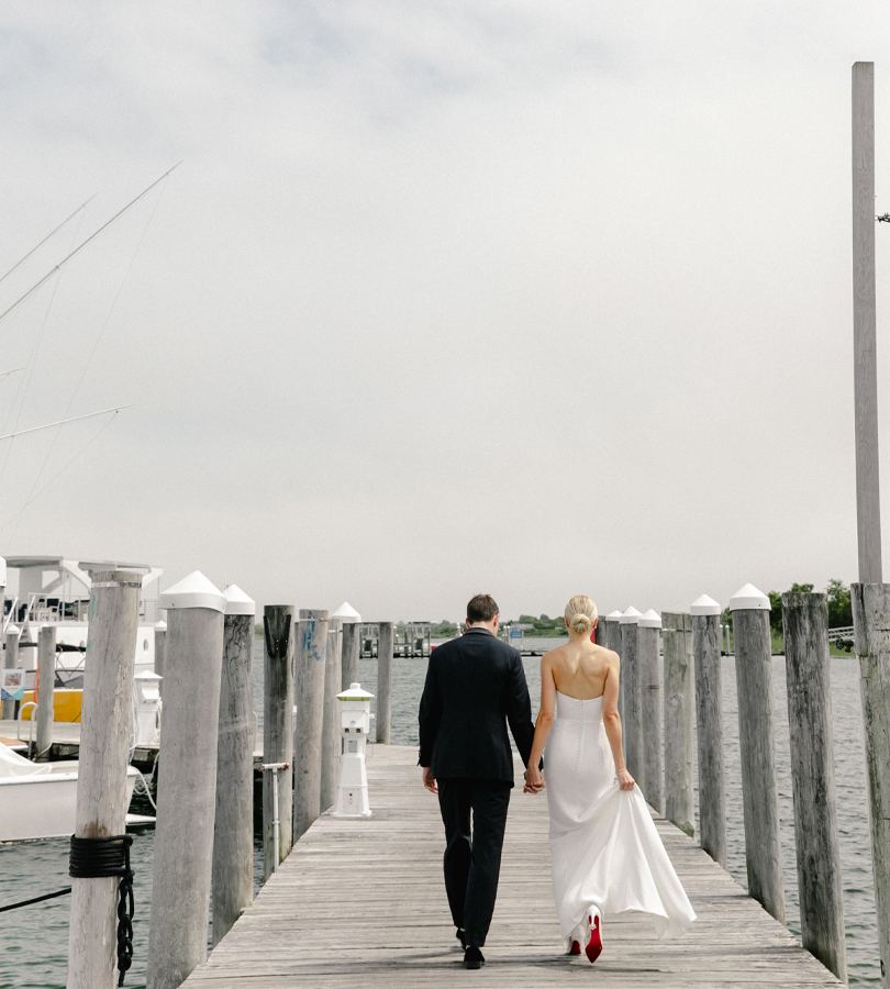 A man in a black suit walks with a lady in white on a dockyard ramp.